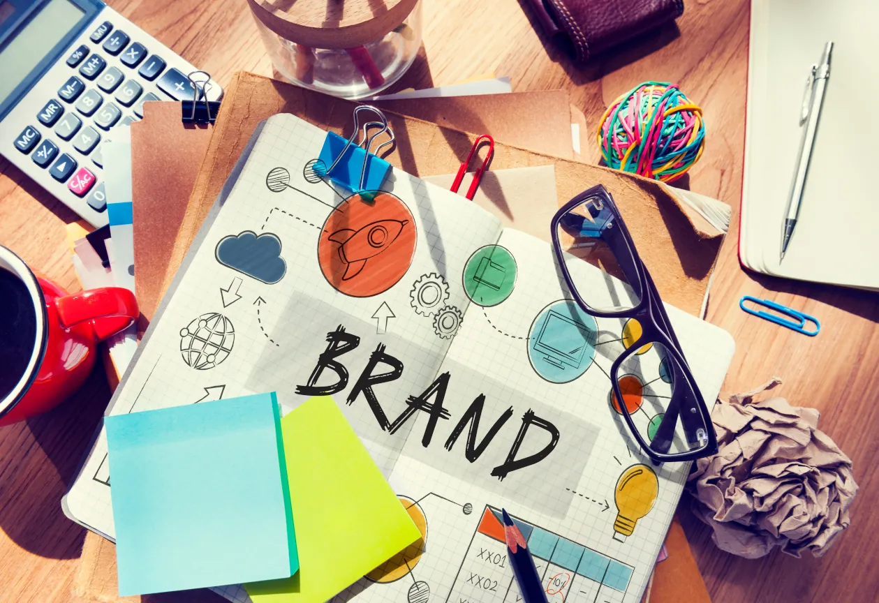 Illustration eines Digital Branding Konzepts mit Skizzen, Farben und Symbolen auf einem Schreibtisch.