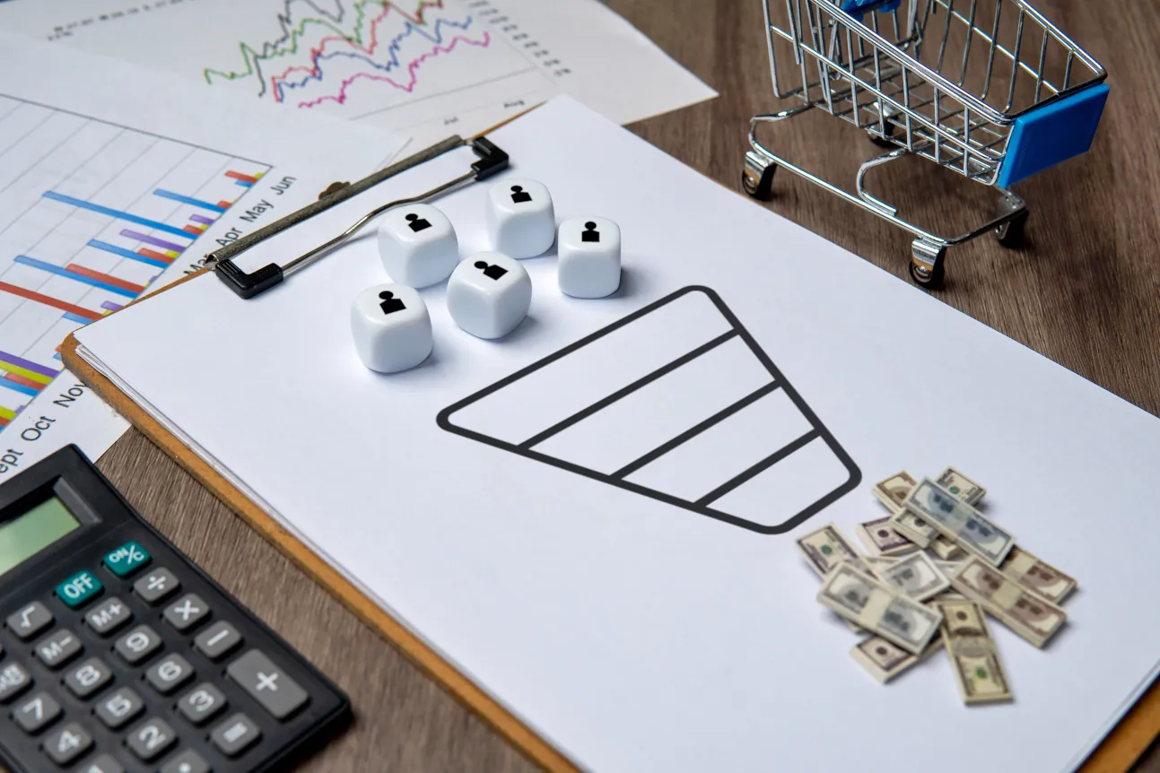 Diagramm eines Marketing Funnels auf einem Clipboard mit Würfeln, Geldscheinen und einem Einkaufswagen, das den Prozess der Kundengewinnung und Konvertierung symbolisiert.