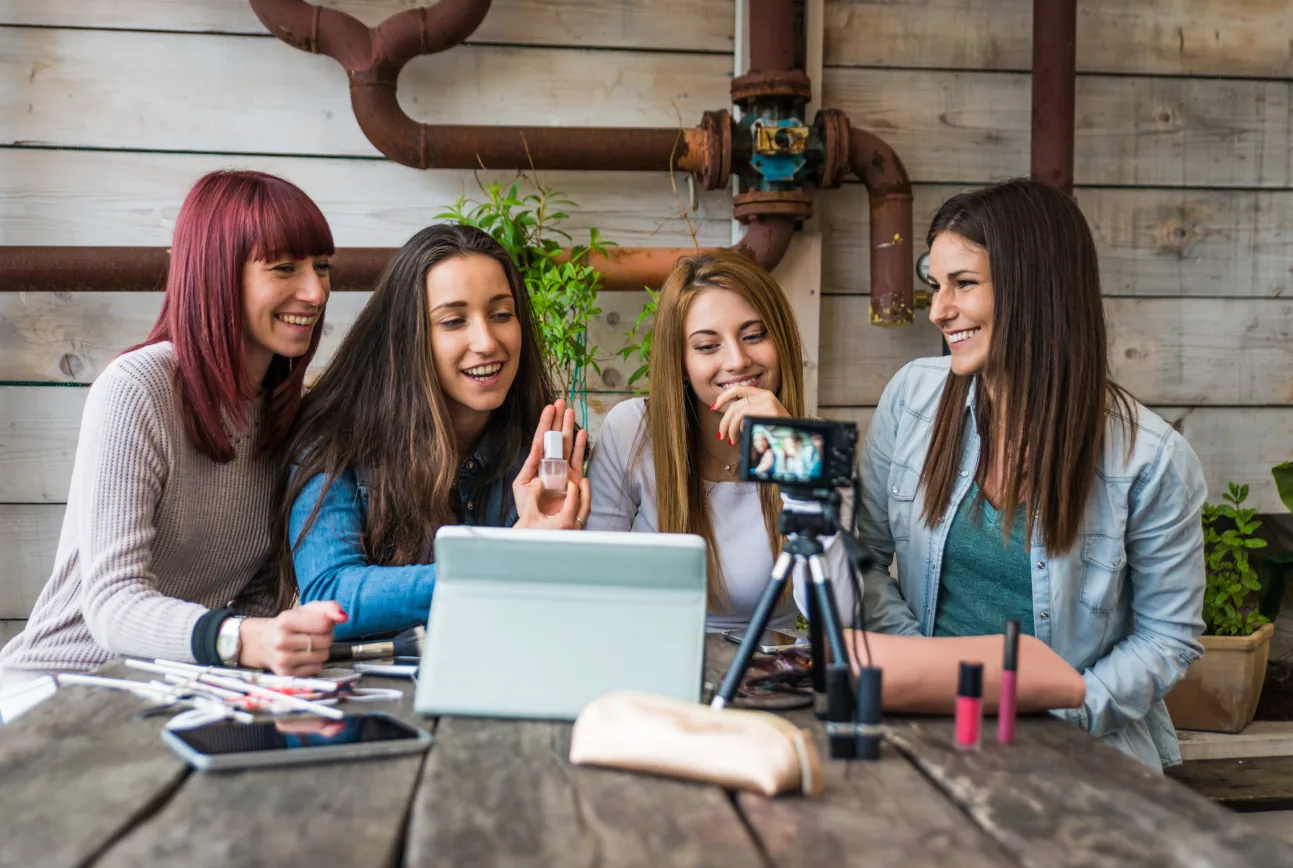 Vier junge Influencerinnen erstellen gemeinsam Content für Social Media, präsentieren Beauty-Produkte und lachen vor einer Kamera im Outdoor-Setting.